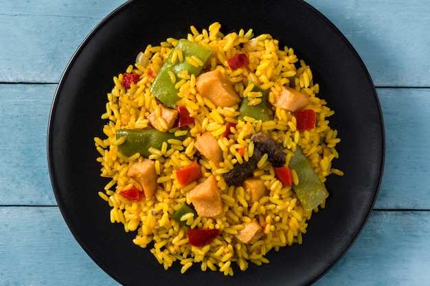 Riz frit au poulet et légumes en plaque noire sur une table en bois bleue se bouchent