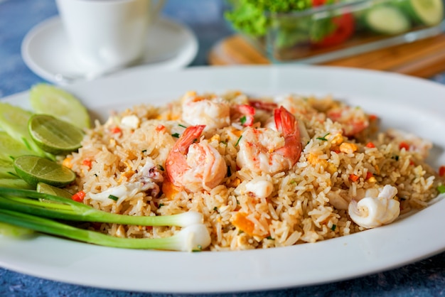 Riz frit aux crevettes avec citron vert et coriandre sur une table bleue avec une tasse de café blanche et des légumes