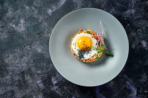 Riz frit dans un wok avec du poulet et des œufs au plat dans une assiette grise sur fond noir. Cuisine de rue asiatique. Vue de dessus. Copier l'espace