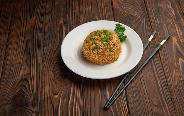 Riz frit de style asiatique avec des oignons frais et des carottes en tranches, des paires de baguettes sur une table en bois foncé, copie espace, vue de dessus du concept alimentaire oriental