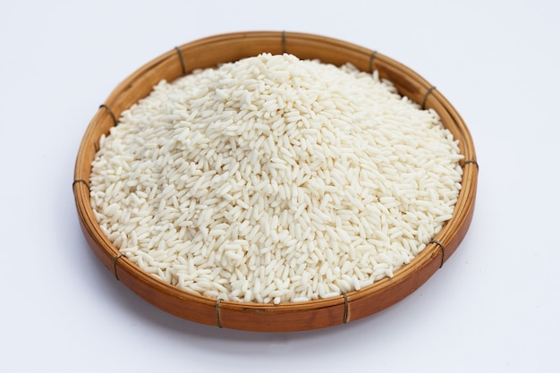 Riz gluant cru dans un panier en bambou sur fond blanc.