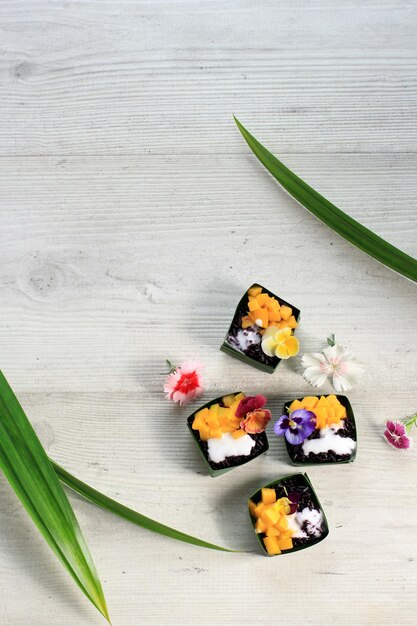 Riz gluant noir à la noix de coco fait maison avec mangue dans une tasse de feuilles de pandan, mise au point sélective avec garniture de fleurs de pensées Edibel, espace de copie sur le dessus