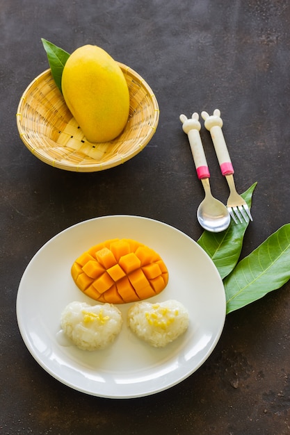 Riz gluant et tranche de mangue mûre sur plaque blanche et panier