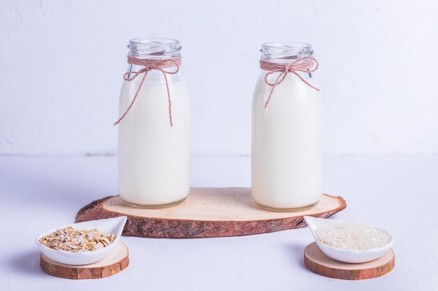 Riz et lait végétalien d'avoine dans des bouteilles en verre sur un support en bois sur fond blanc