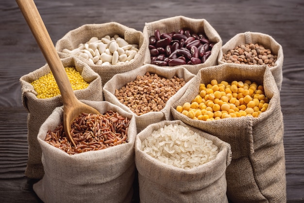 Riz, légumineuses et céréales dans des sacs sur une table en bois sombre.