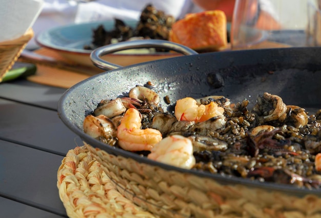 Riz noir aux calmars et crevettes dans une poêle à paella Prêt à manger avec du pain et du vin rouge