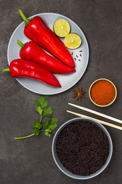 Riz Noir Dans Un Bol Gris. Poivron Rouge Et Citron Vert Dans Une Assiette Grise. Bâtonnets De Bambou Et Poivron Rouge Moulu Dans Un Bol. Mise à Plat.