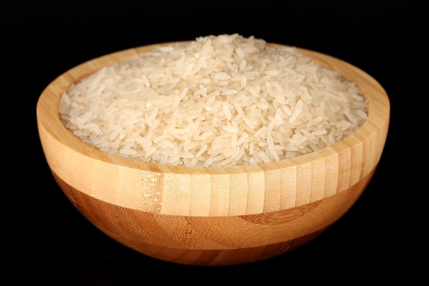 Riz poli blanc dans un bol en bois isolé sur du noir