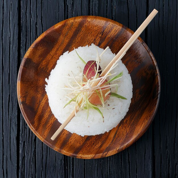 Le riz pour le sushi dans une assiette en bois avec des bâtons sur un fond rustique noir