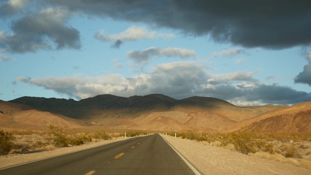 Road trip, conduite automobile de Death Valley à Las Vegas, Nevada USA. Faire de l'auto-stop en Amérique. Voyage sur l'autoroute, atmosphère dramatique, montagne au coucher du soleil et désert de Mojave. Vue depuis la voiture.