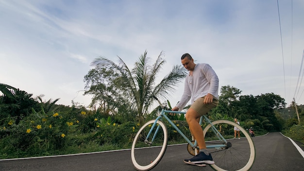 Road trip à vélo L'homme sur un vélo bleu en vêtements blancs sur une route forestière Les hommes motards montent à vélo Cycling Cycle Fix Asia Thailand ride tourism Prendre une photo avec un vélo