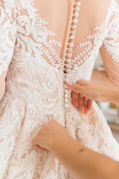 Robe blanche de la mariée aidée à se boutonner par la demoiselle d'honneur