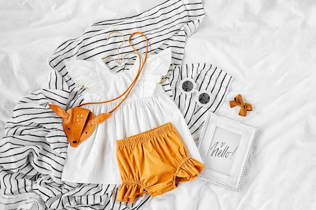 Robe blanche, short orange avec sac à main pour enfants et lunettes de soleil. Ensemble de vêtements et accessoires pour bébés pour les vacances d'été au lit. Tenue de mode pour enfants. Mise à plat, vue de dessus