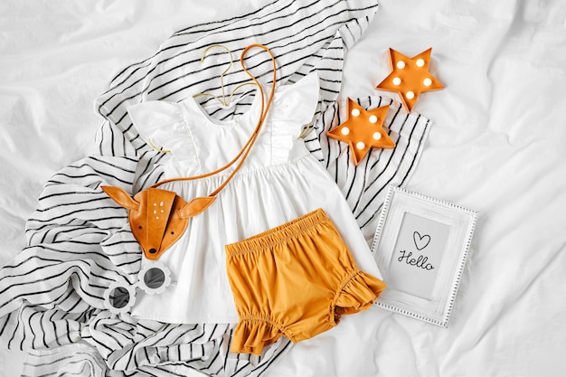 Robe blanche, short orange avec sac à main pour enfants et lunettes de soleil. Ensemble de vêtements et accessoires pour bébés pour les vacances d'été au lit. Tenue de mode pour enfants. Mise à plat, vue de dessus