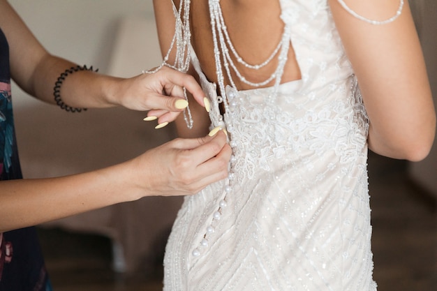 Robe de demoiselle d'honneur blanche qui aide à boutonner les copines