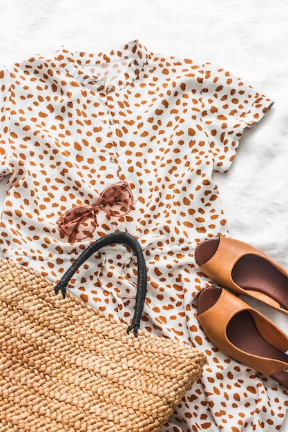 Robe d'été pour femme sac de paille ouvert sandales en cuir et lunettes de soleil sur fond clair vue de dessus