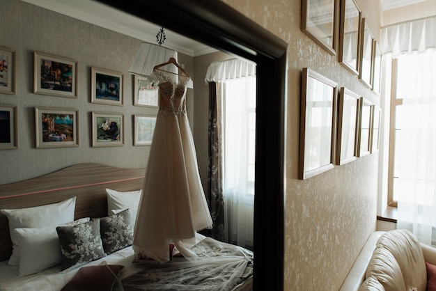 Photo robe de mariée accrochée à un cintre dans la chambre de la mariée du matin