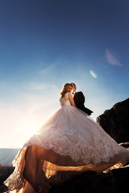 Robe de mariée blanche avec dentelle le marié embrasse la mariée sur les rochers de la joue et le ciel