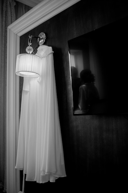 La robe de la mariée est accrochée au mur noir. robe de mariée sur un mur noir, sur une lampe. noir et blanc