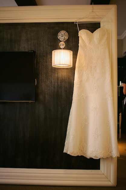 La robe de la mariée est accrochée au mur noir. robe de mariée sur un mur noir, sur une lampe.