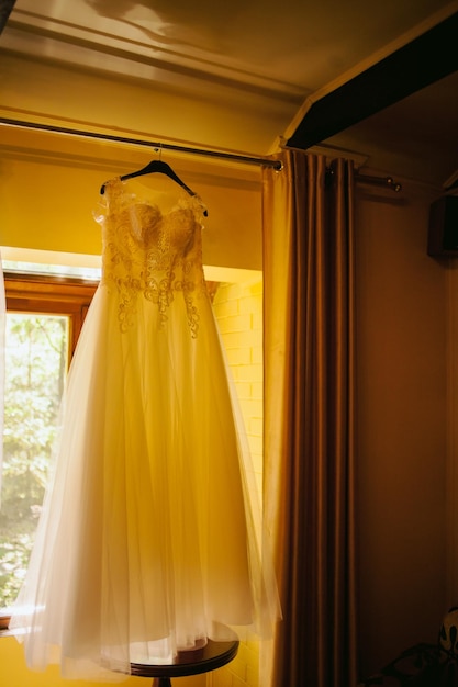 La robe de la mariée est accrochée à la fenêtre. robe de mariée de luxe accrochée à la fenêtre dans une chambre d'hôtel.