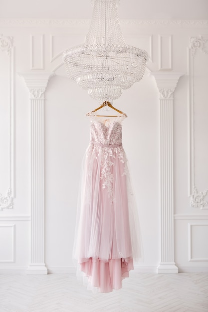 Robe de mariée rose riche se bloque sur un lustre dans une salle blanche