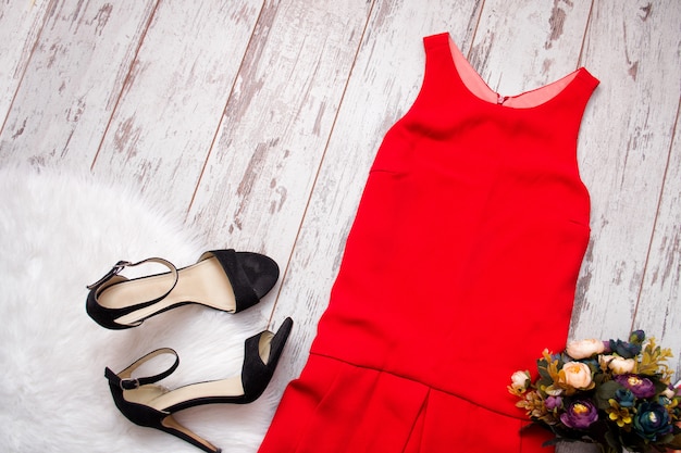 Photo robe rouge, chaussures noires et bouquet. fausse fourrure sur un bois, concept à la mode, vue de dessus