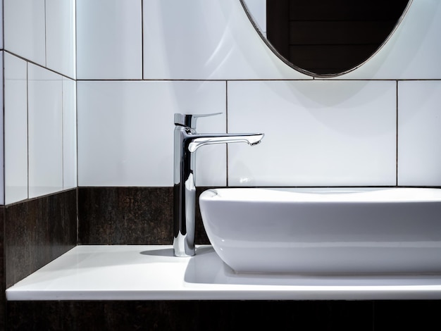 Robinet moderne en acier inoxydable sur un lavabo en céramique blanche dans la salle de bain avec miroir Lavabo en céramique de forme rectangle propre sur une décoration de comptoir en marbre avec des carreaux de mur à motif de rouille de style loft