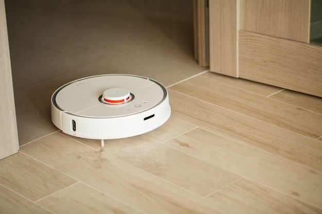 Robot aspirateur fonctionne sur un plancher en bois dans un salon.