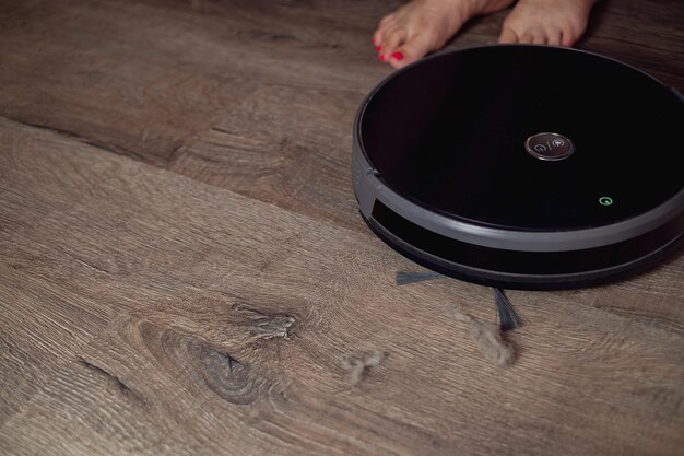 Un robot aspirateur nettoie le salon la fille a enlevé ses pieds pour laisser le robot