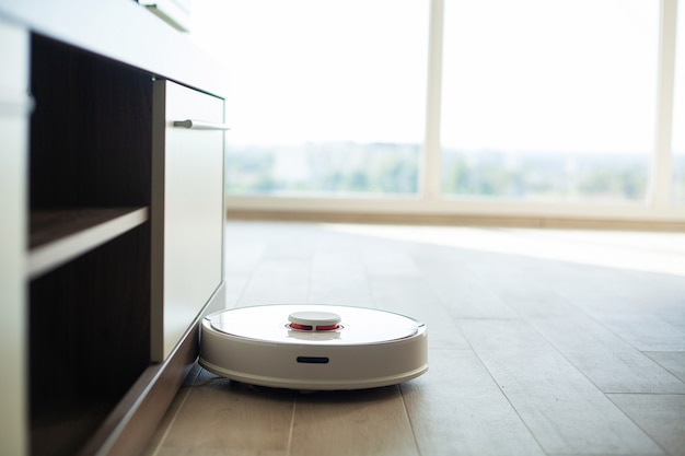 Un robot aspirateur tourne sur un plancher de bois dans un salon