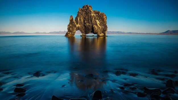 un rocher dans l'eau avec un coucher de soleil en arrière-plan