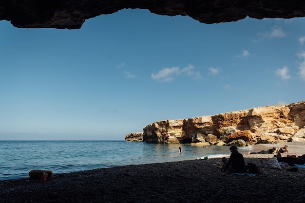 Des rochers massifs s'enfoncent dans l'eau sur une plage de galets