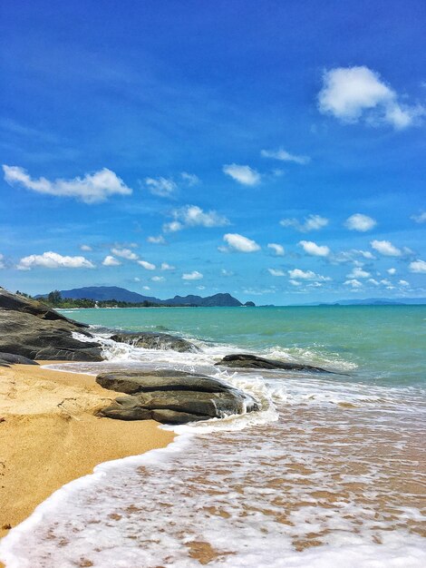 Des rochers noirs sur la plage des vagues dans la mer le ciel est de beaux nuages