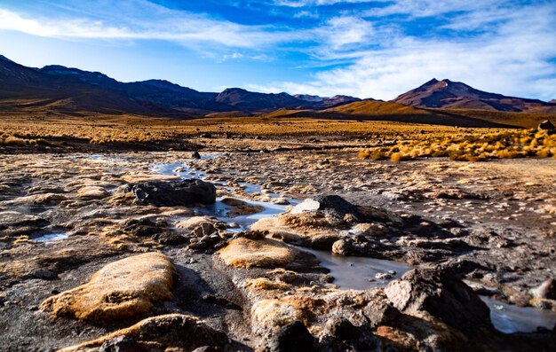 Des rochers sur une terre humide et des montagnes en arrière-plan et un ciel bleu nuageux