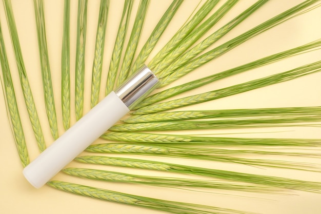 Roller crème anti-âge sur fond blanc avec des épillets de blé vert