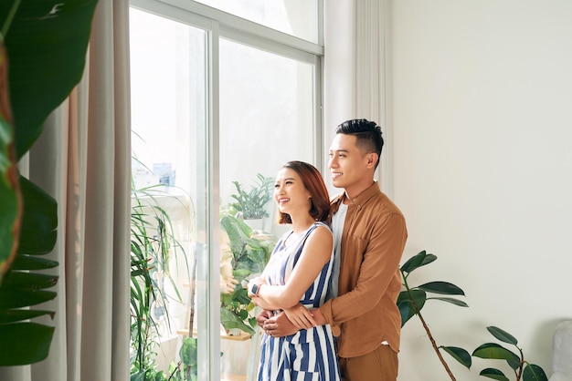 Romantique heureux jeune couple debout et s'embrassant tout en se tenant près de la fenêtre