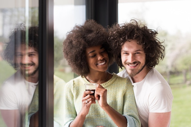 romantique heureux jeune couple multiethnique appréciant le café du matin près de la fenêtre dans leur maison de luxe