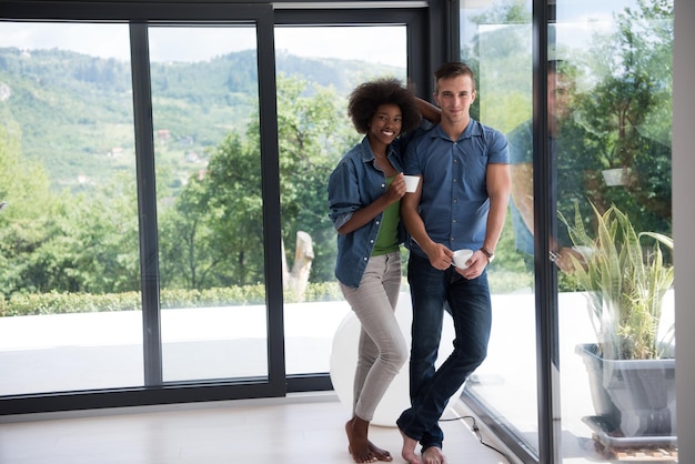 romantique heureux jeune couple multiethnique appréciant le café du matin près de la fenêtre dans leur maison de luxe