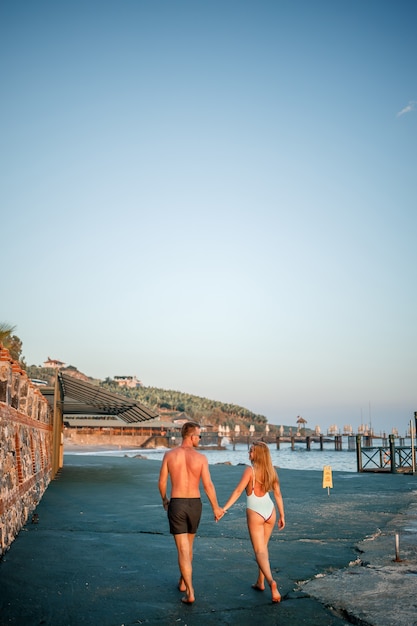 Romantique jeune couple amoureux marchant ensemble au coucher du soleil le long de la plage méditerranéenne. Vacances d'été dans un pays chaud. Heureux couple marié en vacances en Turquie. Mise au point sélective