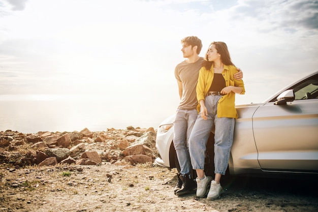 Romantique jeune couple séduisant regardant le coucher de soleil et s'embrassant avec une voiture de sport.