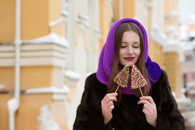 Romantique jeune femme brune en foulard violet tenant des bonbons de Noël colorés