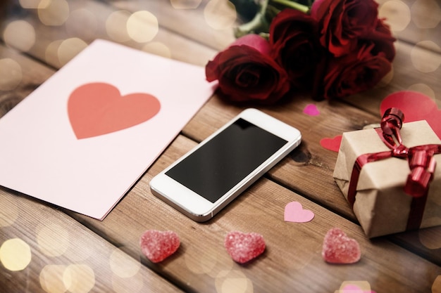 romantisme, jour de la Saint-Valentin et concept de vacances - gros plan du smartphone, boîte à cadeaux, roses rouges et carte de vœux avec des bonbons en forme de cœur sur du bois (effet vintage)