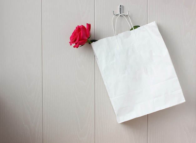 Rose rose dans un sac en papier sur un crochet sur un mur léger