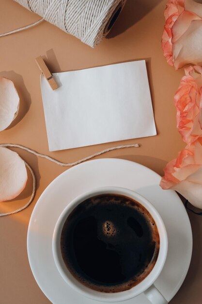 Photo rose rose tendre avec une tasse de café blanche sur fond beige note de papier vide rose pastel romantique
