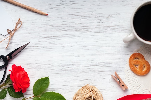 Rose rouge, café, ciseaux et autres petits objets sur table en bois blanc, vue de dessus