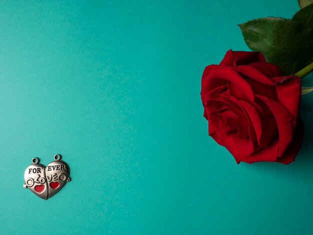 Une rose rouge avec des pétales verts qui se trouve sur le côté et deux parties d'un cœur en argent avec une inscription sur le vert