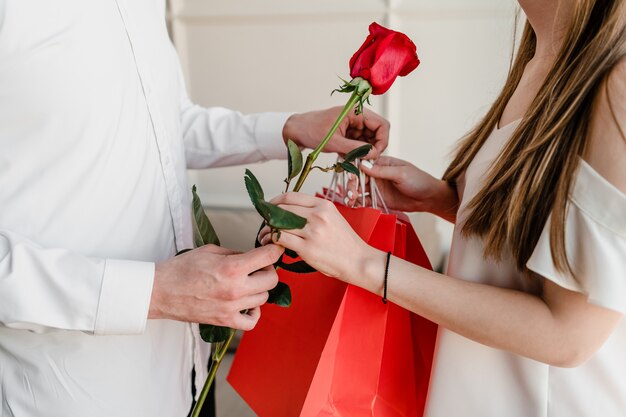 Rose rouge et sacs à provisions dans les mains de l'homme et de la femme à la maison