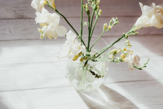 Des roses blanches se tiennent dans un vase sur des planches en bois blanches