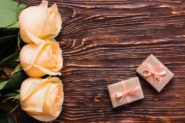 Roses fraîches et un couple de cadeaux emballés sur bois, vue de dessus